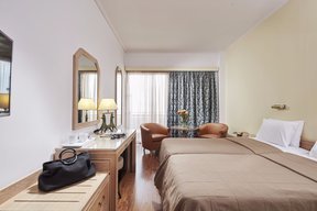Triple bedroom at Candia Hotel with beds, desk and chair and sitting area next to the balcony
