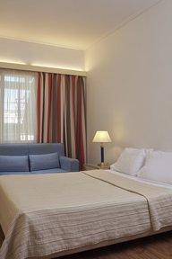 Bedroom with a double bed, blue sofa and striped drapes at Candia Hotel