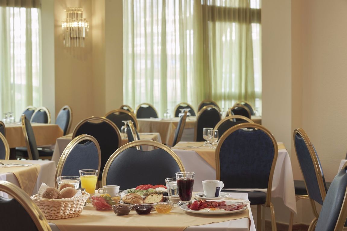 Breakfast hall with table and chairs and plates of food at Candia Hotel