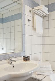 White tiled bathroom with sink and towel rack at Candia Hotel