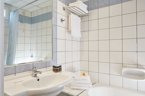 Bathroom of Candia Hotel with white tiles, bathtub with shoer curtain, sink and towel racks