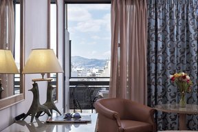 Desk with lamp and glasses and balcony with city view at Candia Hotel