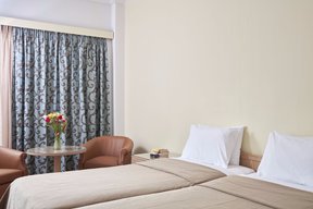 Bedroom with twin beds, bedside table, sitting area and blue design drapes at Candia Hotel