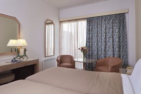 Bedroom with two beds and sitting area with two armchairs plus desk at Candia Hotel