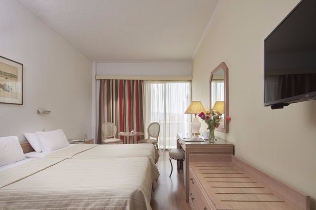 Bedroom with two beds, desk, sitting area, TV and striped drapes at Candia Hotel